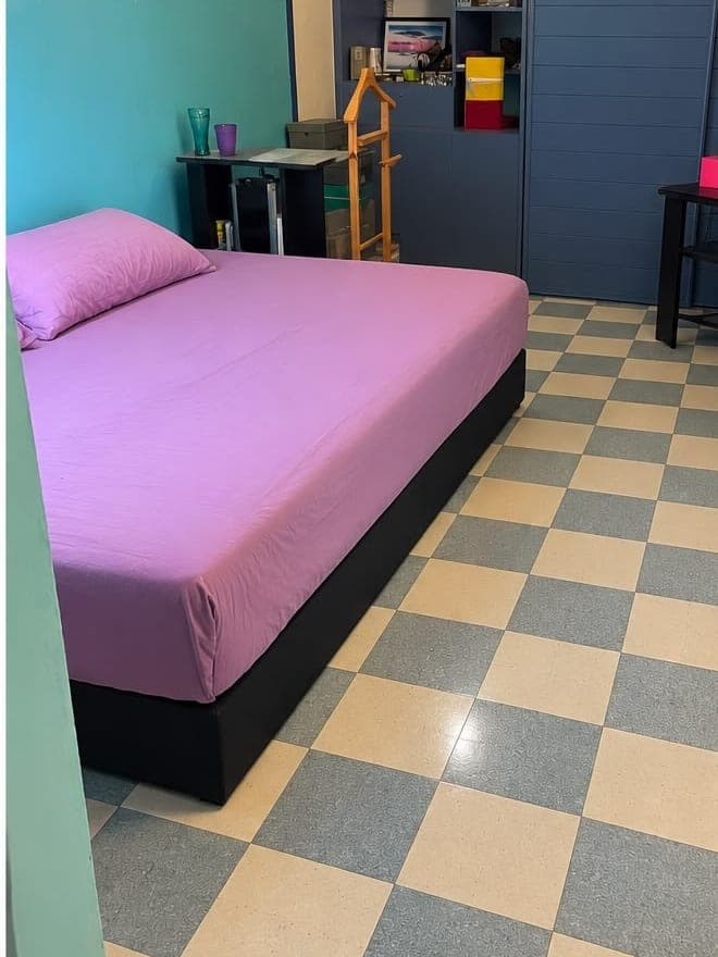 La même chambre après intervention : lit refait d'un drap housse mauve, sol en damier dégagé et lavé