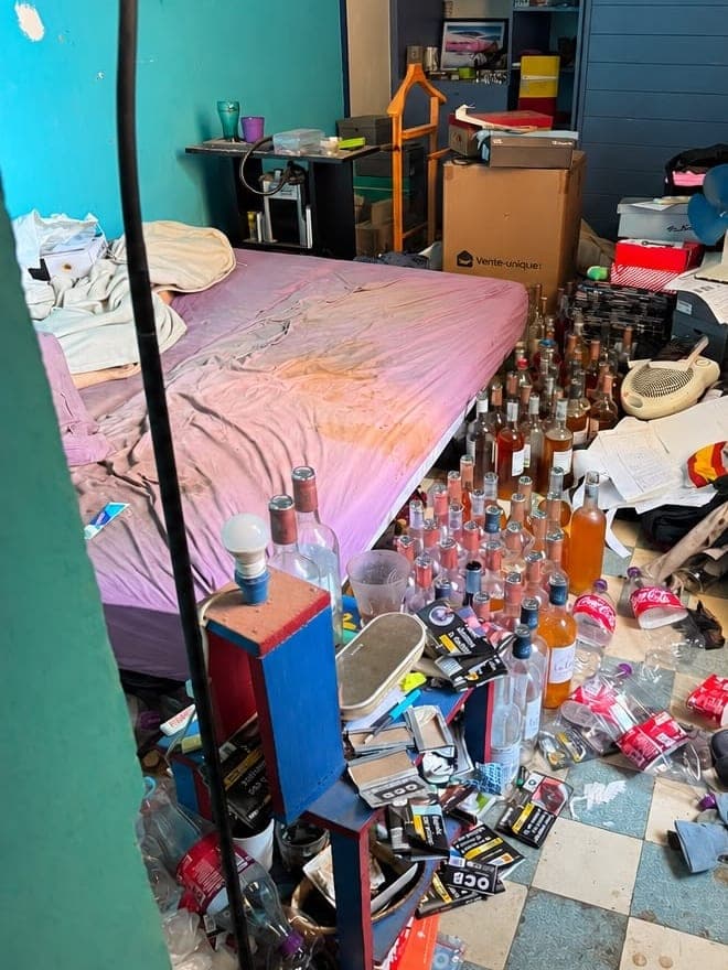 Chambre aux murs turquoise avant intervention : lit défait, bouteilles, cartons et papiers répandus sur le sol en damier