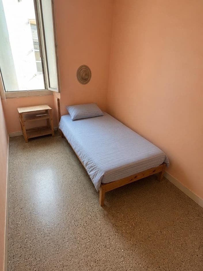 La même chambre aux murs saumon après intervention : lit fait d'une housse rayée, chevet en bois, sol granito dégagé