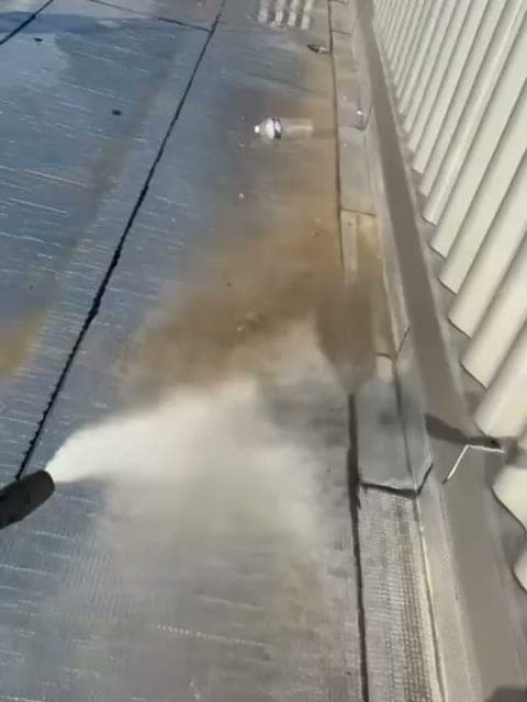 Jet d'eau haute pression sur une toiture-terrasse, au pied d'un bardage ondulé