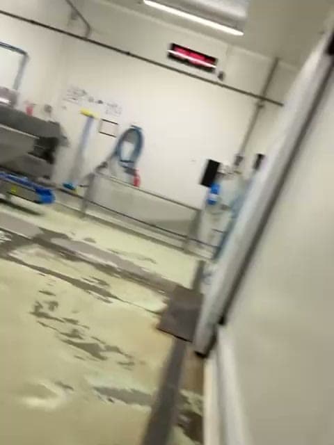 Atelier de production aux murs blancs, cuve inox et tuyaux, sol carrelé mouillé en cours de lavage