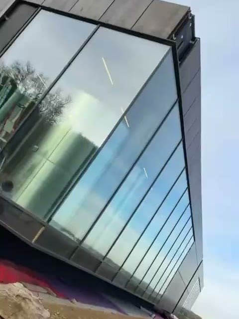 Façade vitrée d'un bâtiment neuf à bardage sombre, cône de chantier au pied