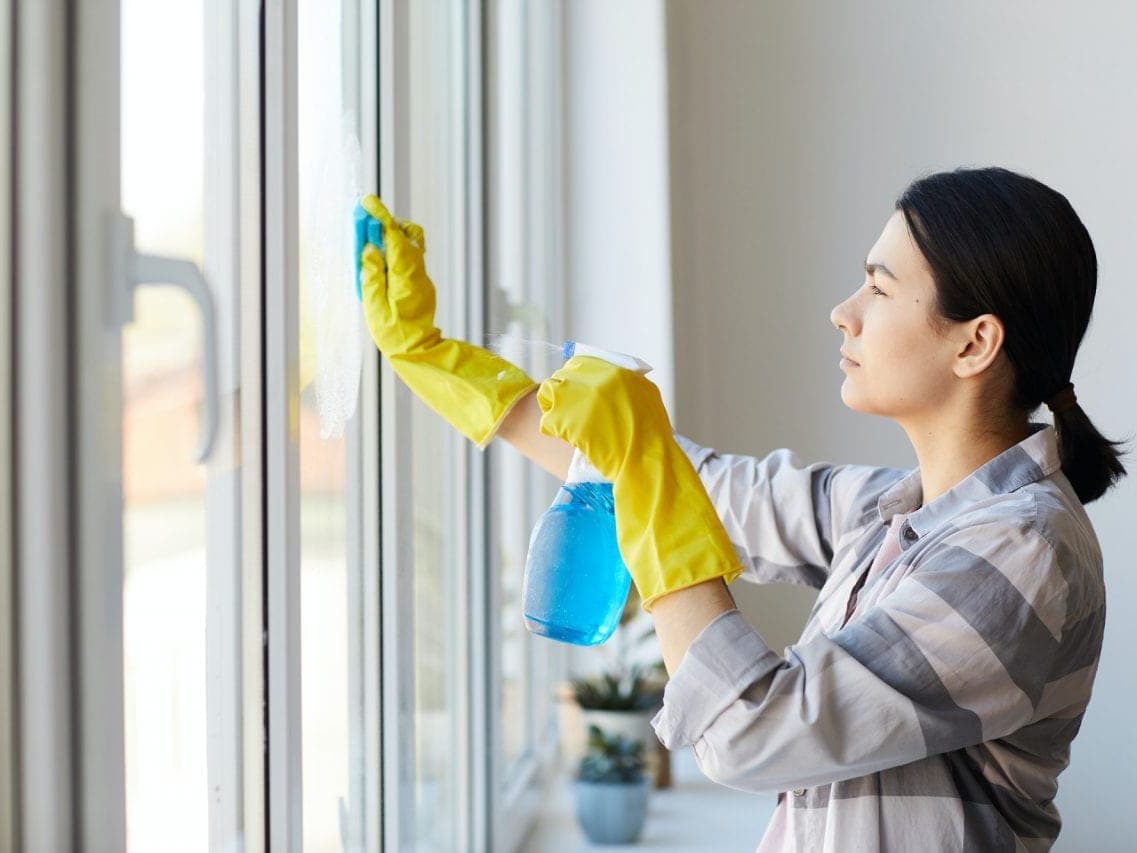 Femme en gants jaunes qui nettoie une fenêtre au pulvérisateur et au chiffon, vue de profil
